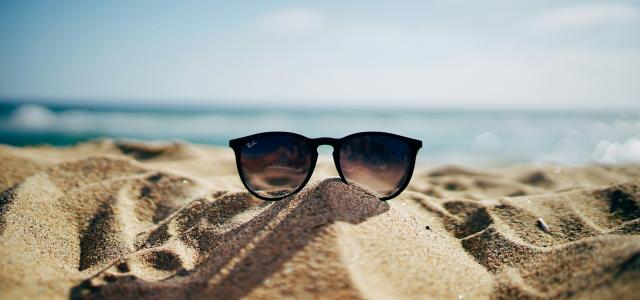black Ray-Ban Wayfarer sunglasses on beach sand by Ethan Robertson courtesy of Unsplash.
